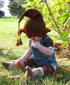 a small child sitting in the grass wearing a knitted hat