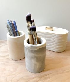 two white containers with brushes in them sitting on a table next to another container filled with pens and pencils