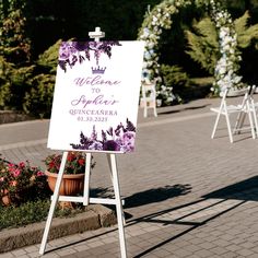 a welcome sign with purple flowers on it in front of some chairs and tables outside