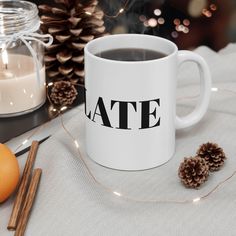 a white coffee mug sitting on top of a table next to an orange and some pine cones