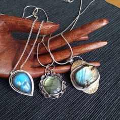 "Pendants of the collection ~NINFEA~ Stunning labradorite pieces, each of a different hue of colour ranging from deep blue to green and gold. The collection is inspired by water and by the beautiful plants and flower that grow into it, such as water lilies, \"nifea\" in Italian. All pieces are one of a kind and made with love. Here a full description of each piece: 1) Large piece of labradorite (3 x 2 cm) with green and golden hues set in a mix of silver and brass. The pendant is roughly 4.5 cm long and 3.5. cm wide. The back of the pendant features sun and cloud shaped cuts, thus showing the beauty of the stone from the back too. If desired, the pendant can be complemented by one of the two available types of chain. 2) Sleek pendant with a deep blue, tear-shaped labradorite piece. The pen Hand Forged Silver Necklaces In Nature-inspired Style, Hand Forged Silver Nature-inspired Necklace, Hand-forged Silver Nature-inspired Necklace, Bohemian Hand Forged Sterling Silver Jewelry, Labradorite Jewelry With Soldered Details As Gift, Silver Nature-inspired Jewelry, Blue Labradorite Bohemian Jewelry, Silver Teardrop Necklaces With Unique Variations, Nature-inspired Silver Brass Necklaces