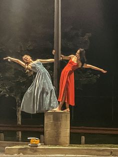 two women in red and blue dress standing on top of a pole with their arms stretched out