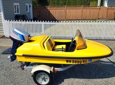 a small yellow speed boat parked in front of a white picket fence