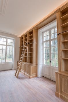 an empty room with wooden shelves and ladder in the center, next to two windows