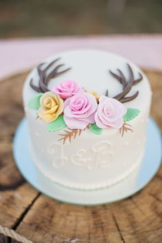 a wedding cake decorated with flowers and antlers on a wooden sliced tablecloth