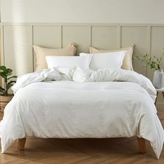 a bed with white linens and pillows in a small room next to a potted plant