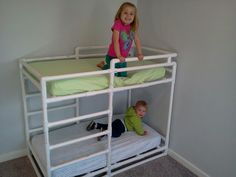 two children are standing on the bottom bunk of a white bunk bed with green sheets