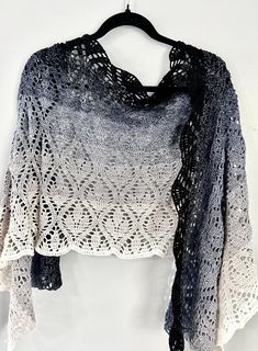 a black and white crochet shawl hanging on a wall next to a wooden hanger