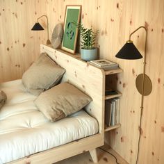 a bed with pillows and two plants on top of it next to a book shelf