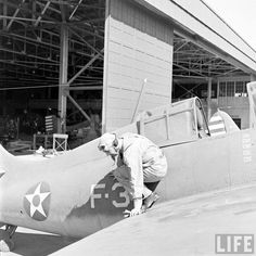 an old black and white photo of a man working on a plane