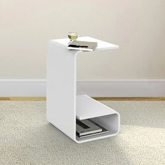 a small white table with a magazine rack on it and a glass in the middle