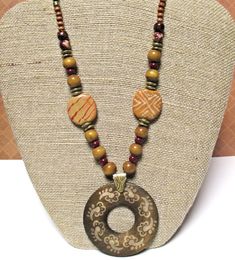 Wood Pendant Necklace on Waxed Linen Cord  16 to 21 inches (or shorter on request) with 2 inch round pendant They say if you can remember the Sixties, you weren't there. But I was there, and I do remember the fabulous, fun, tribal style jewelry that was popular then - and it's quite trendy today!  This red and brown pendant necklace features: * 2 inch round dark brown wood pendant covered with light tan symbols * anti-tarnish brass bail * dark brown waxed linen cord  * gorgeous golden tan Kazuri beads painted with white and red designs * wood beads in various sizes and tones * glass pearls in deep red * antiqued gold metal spacers * Nunn Design antiqued gold plated textured jump rings * gold plated chain * gold plated lobster claw clasp This bohemian jewelry can be worn at anywhere from 16 Bohemian Brown Beaded Round Necklaces, Bohemian Brown Beaded Necklace, Brown Amulet Necklaces With Large Beads, Brown Round Bead Necklaces For Festivals, Adjustable Brown Beaded Necklace With Round Pendant, Brown Polished Beads Necklaces For Festivals, Brown Wooden Beads Amulet Necklace, Traditional Brown Beaded Necklaces For Gifts, Adjustable Wooden Beads Necklace For Festivals