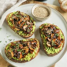 three pieces of bread with mushrooms and avocado on it next to a bowl of sesame seeds