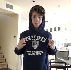 a young man wearing a nypd hoodie standing in front of a dining room table