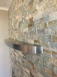 a metal shelf mounted to the side of a brick wall with stone veneers