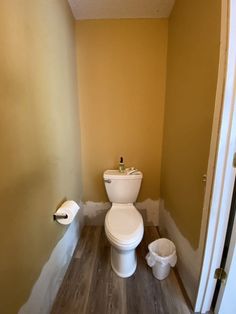 a white toilet sitting inside of a bathroom next to a wooden floor and wall with paint on the walls