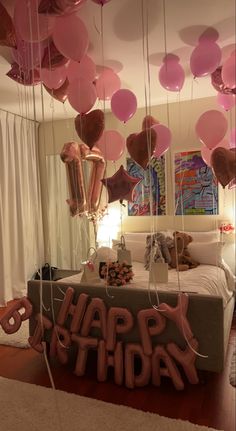 balloons and streamers are hanging from the ceiling in front of a bed that has a happy birthday sign on it