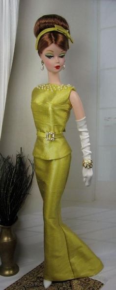 a doll in a yellow dress and white gloves is standing next to a potted plant