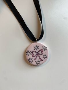 a pink necklace with black stars and a bow on the front is hanging from a black ribbon