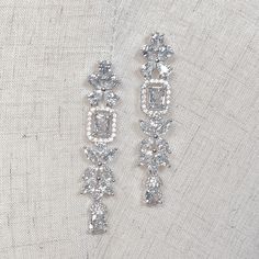 two pairs of diamond earrings sitting on top of a white cloth