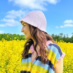 a woman standing in front of a field of yellow flowers wearing a pink and blue hat