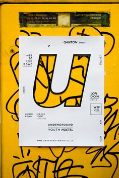 the letter u is written in black and white on a yellow wall covered with graffiti