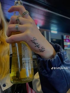 a woman holding up a beer bottle with the word happy written on her arm and wrist