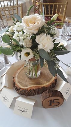 a vase with flowers is sitting on top of a wooden slice at the center of a table