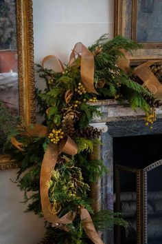 a christmas wreath with pine cones and greenery on the mantle in front of a fireplace