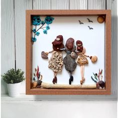 some rocks and plants in a wooden frame on a white shelf next to a potted plant