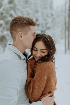 a young man and woman are hugging in the snow while they stand close to each other