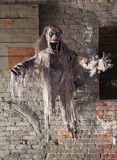 a creepy figure hanging from the side of a brick wall