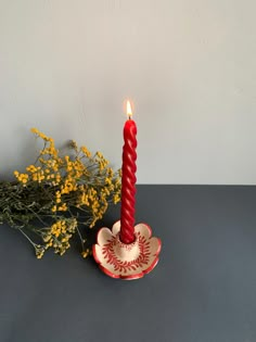 a red candle sitting on top of a table next to yellow flowers