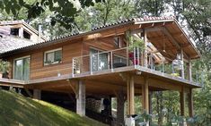 a large wooden house sitting on top of a lush green hillside next to a forest