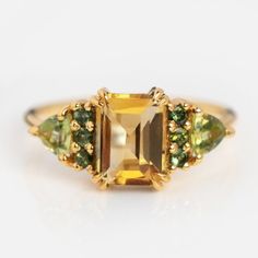 a yellow gold ring with green and brown stones on the sides, surrounded by other gems