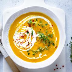 a white bowl filled with carrot soup and topped with sour cream, garnished with fresh herbs