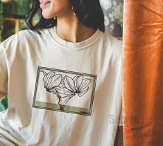 Cyclamen Floral Vintage Artwork Tee Ivory 1920 Cyclamen by Julie de Graag Vintage style Tee ( Ivory ) ✦  About ・Crew Neck Classic style Retro T-shirt ・100% ring-spun US cotton for extra comfort ・Soft-washed, garment-dyed fabric  ・Comfort Colors Tees are made using 100% US cotton that is ethically grown and harvested Protocol ensuring ethical and sustainable means of production. ・Check out sizing chart for a desired fit ✦  Print Type ・Direct to Garment printing is used for max comfort ・Ink is printed right into garment so colors may achieve a desirable slight retro color fade after many washes ・Graphic print size may vary slightly ✦  Wash + Care ・Machine wash: cold (max 30C or 90F) with like colored garments; Do not bleach; Tumble dry: low heat; Iron, steam or dry: low heat; Do not dryclean Artistic White Relaxed Fit Shirt, Art Tshirt, 90s Shirts, Retro Clothing, Retro T Shirt, Tshirt Art, Comfort Colors Tee, Vintage Artwork, Retro Color