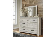 a white dresser and mirror in a room with wood wallpaper on the walls behind it