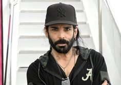 a man with long hair and beard wearing a hat standing in front of some stairs