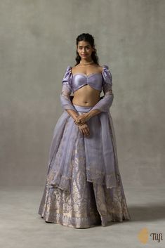 "\nJuliette\u00a0\u00a0\n\nIn an enchanting palette, this lehenga set combines exquisite aari-embroideries and roopa sona zari Kadhua weaves in designs inspired by the ornate and whimsical art and architecture of Rococo. The blouse has a ruched bodice, a classic wide-cut neckline, puffed sleeves, and delicate viscose-organza trimmings along the edges, inspired by the lacework\u00a0which was\u00a0abundantly used\u00a0in Rococo fashion. The gossamer Odhani is\u00a0encrusted with hand-embroidered vines and finished with playful jewel-like tassels.\u00a0\n\n\n Color\u00a0- A\u00a0charming shade of Lavender\n\n Fabric\u00a0- Lehenga skirt in pure satin\u00a0silk, blouse in\u00a0pure\u00a0satin silk with viscose-organza trimmings, and\u00a0Odhani in pure silk organza\u00a0\u00a0\n\nTechnique\u00 French Rococo Art, Define Feminine, Rococo Fashion, Feminine Wardrobe, Brocade Blouses, Lehenga Skirt, Aari Embroidery, Ruched Bodice, Silk Brocade