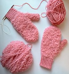 pink knitted mittens, gloves and ball of yarn laid out on a table