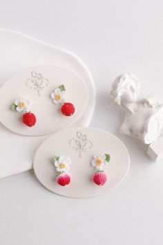 two white plates with strawberry shaped earrings on them