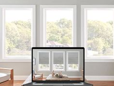 an open laptop computer sitting on top of a wooden table in front of three windows