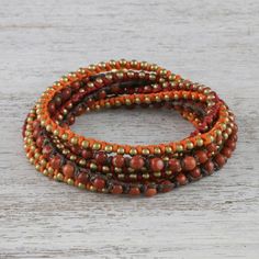 For a festive and delightfully bohemian addition to your wardrobe this wrap bracelet is designed and crafted by Thai artisan Tiraphan Hasub. She hand-braids red orange and brown lengths of polyester cord beaded with red jasper and gleaming brass. The wrap bracelet closes with an adjustable button clasp accentuated by ringing brass bells. Bohemian Wrap Bracelet With Round Beads For Meditation, Bohemian Adjustable Wrap Bracelet With Round Beads, Hippie Wrap Bracelet With Round Beads For Festivals, Bohemian Orange Beaded Bracelets With Round Beads, Adjustable Bohemian Wrap Bracelet With Round Beads, Adjustable Orange Beaded Spiritual Bracelet, Bohemian Orange Bracelets With Colorful Beads, Hippie Style Wrap Bracelet With Round Beads For Festivals, Orange Bohemian Bracelets With Colorful Beads