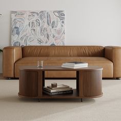 a brown leather couch sitting next to a table with books on it and a painting in the background