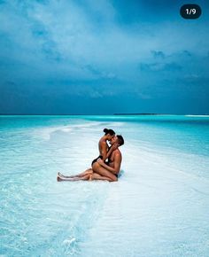 two people are sitting on the beach in the water and one person is kissing her