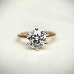 an engagement ring with a single diamond in the center on a white surface, close up