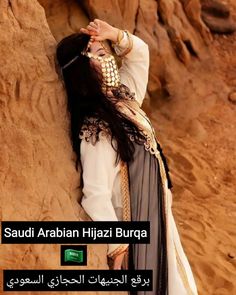 a woman leaning against the side of a rock wearing a white and black dress with gold accents