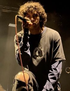 a young man holding a microphone up to his ear while standing on stage with other people behind him