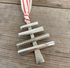 a silver christmas tree ornament hanging on a wooden table with red and white ribbon